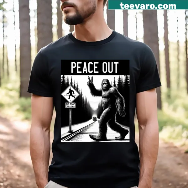 Graphic T-shirt featuring Bigfoot giving a peace sign while crossing a road